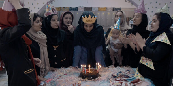 Young woman in a crown looking at a birthday cake, surrounded by other young women