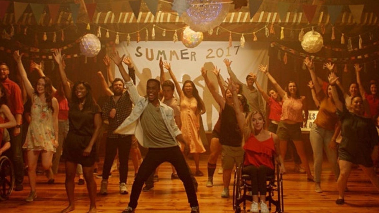 A school dance in front of a Summer 2017 banner, fronted by a boy standing on the left and a girl in a wheelchair on the right