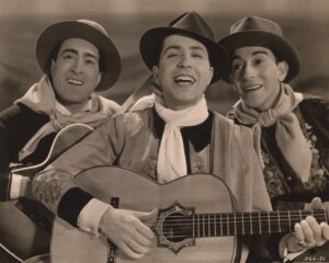Carlos Gardel singing with a guitar and flanked by two other men