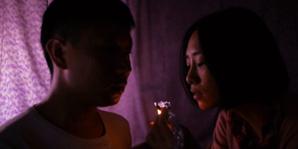 A man and a woman with a pipe between them in a purple-hued room