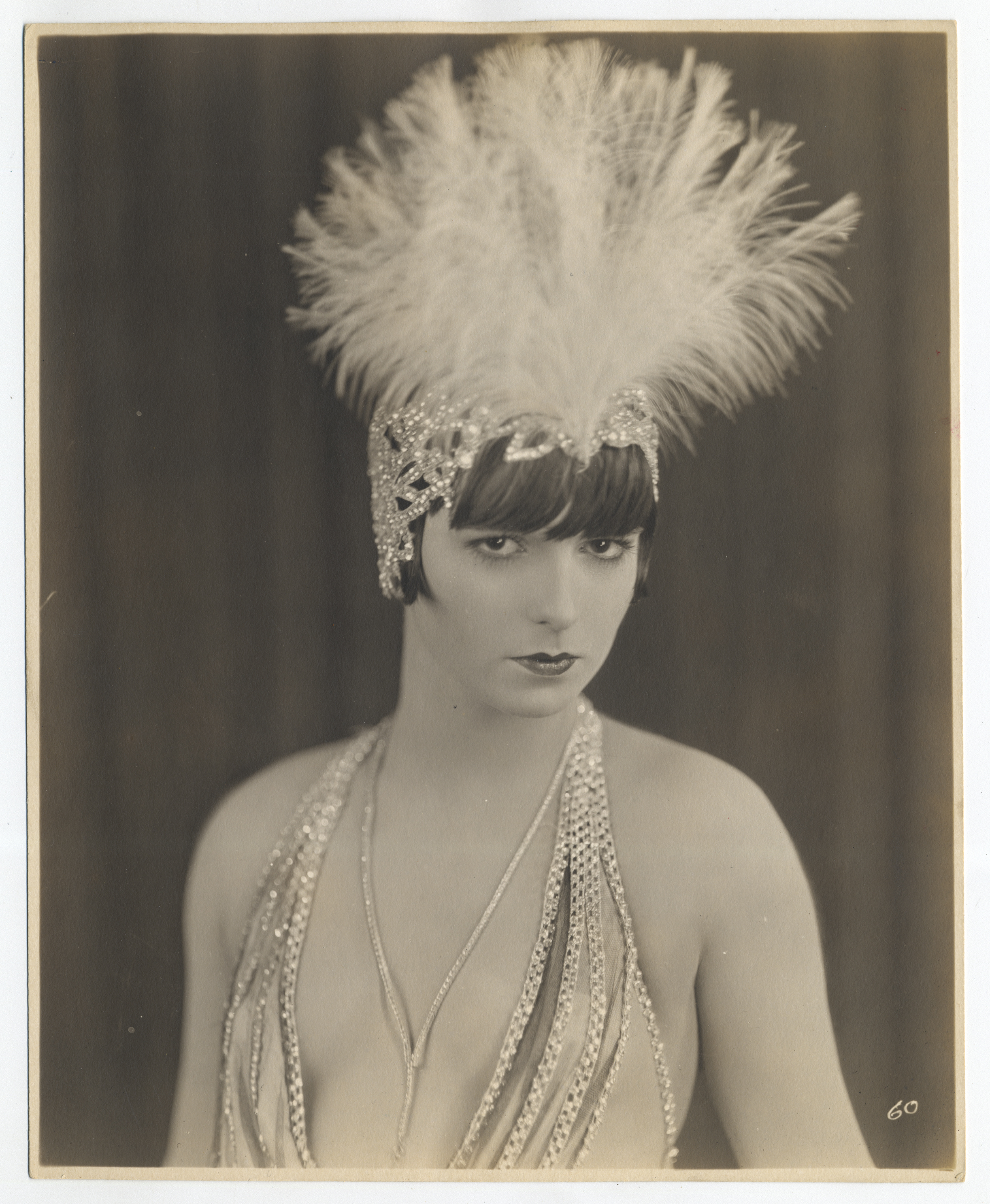 Photo of Louise Brooks in medium shot, wearing a white feathered headdress, looking at camera