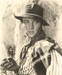 Rudolph Valentino in a hat and holding a cigarette, looking to the left of the camera