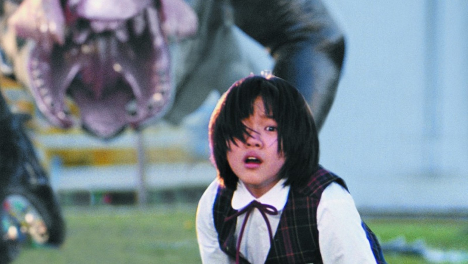 A young girl in a school uniform crouches while a monster menaces in the background