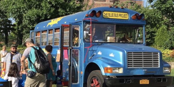 A blue bus parked, with children and adults outside of it