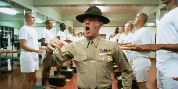 An army drill sergeant yelling while flanked by cadets in basic training