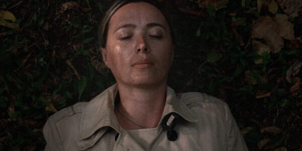A woman lies down with her eyes closed, outside in a bed of leaves
