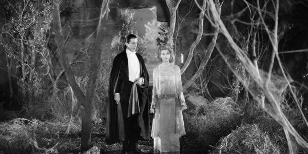 Dracula the vampire and a woman walk in a cobwebbed forest