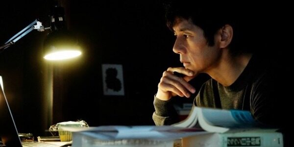 A man sits pensively thinking in a dark room next to a lamp