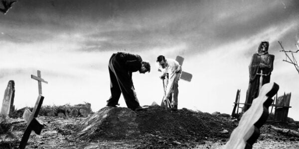Two men dig up a grave on an early morning hillside