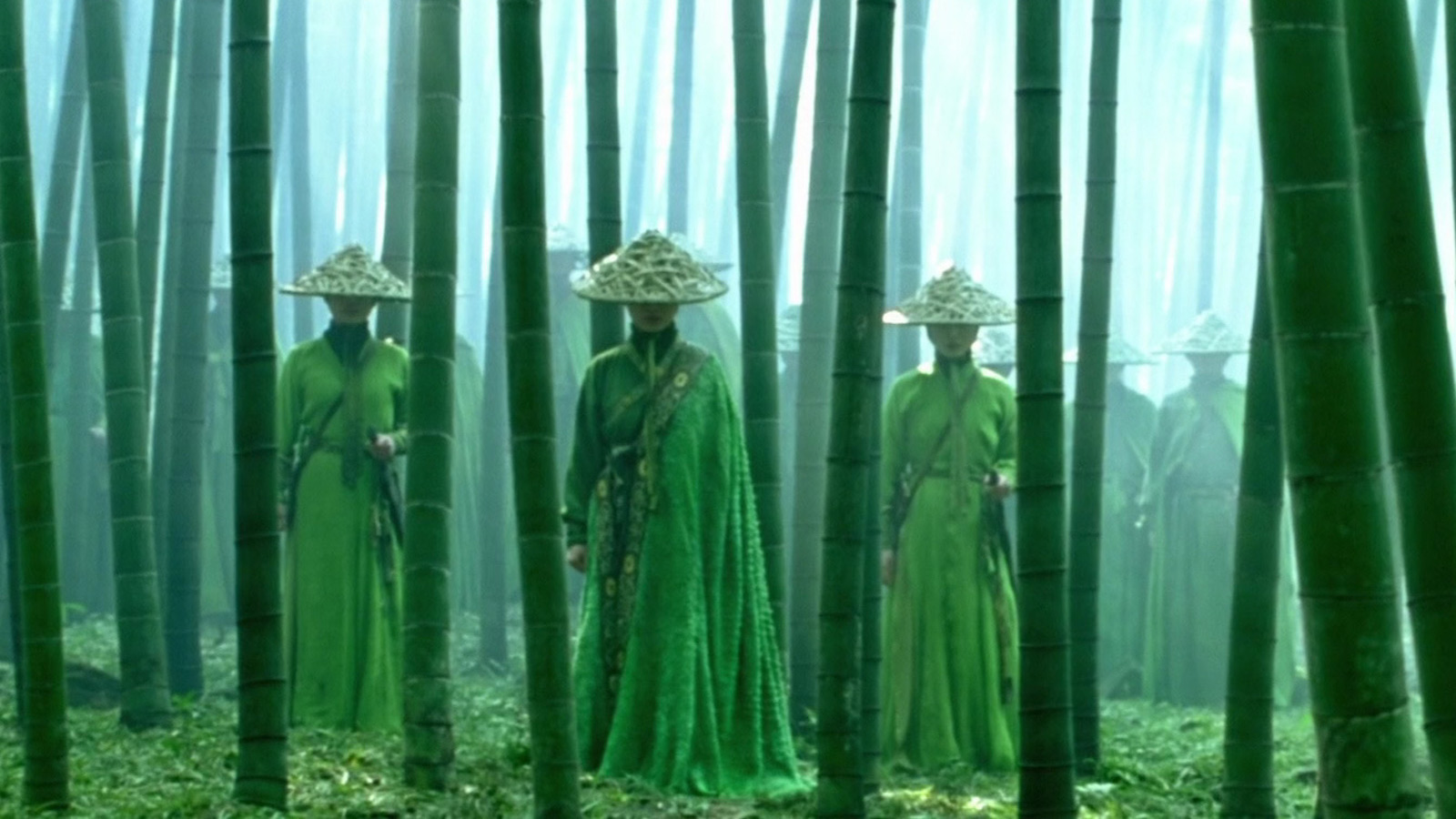 A line of emerald green-dressed assassins, their faces hidden under hats, stands in a bamboo forest facing the camera