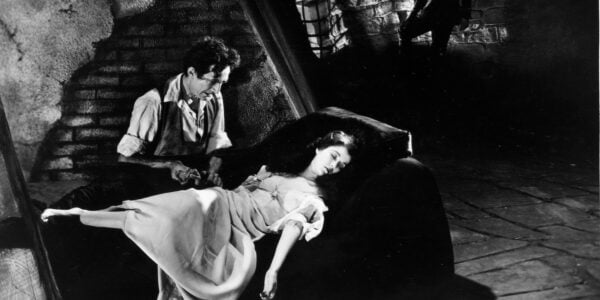A man hovers sinisterly over a woman lying asleep in a dark basement