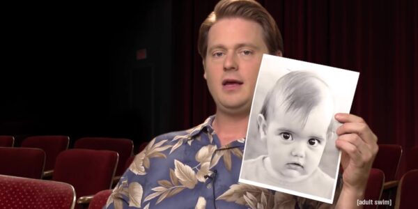 A man holds up a picture of a baby while talking to camera