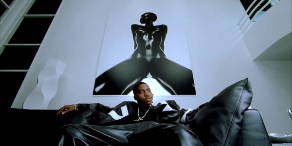 A man sits on a black couch below a baroque framed art work of a sexualized woman