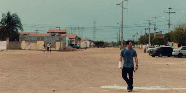 A man wearing a cast on one arm walks through a desolate town.