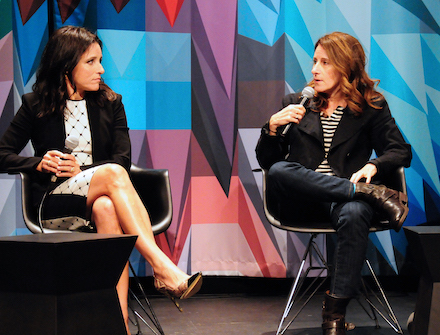 Two women—star Julia Louis-Dreyfus and writer-director Nicole Holofcener— talk to each other onstage at Museum of the Moving Image in front of the colorful curtain.