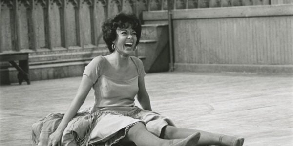 A smiling woman sits on the floor, taking a break from dancing.