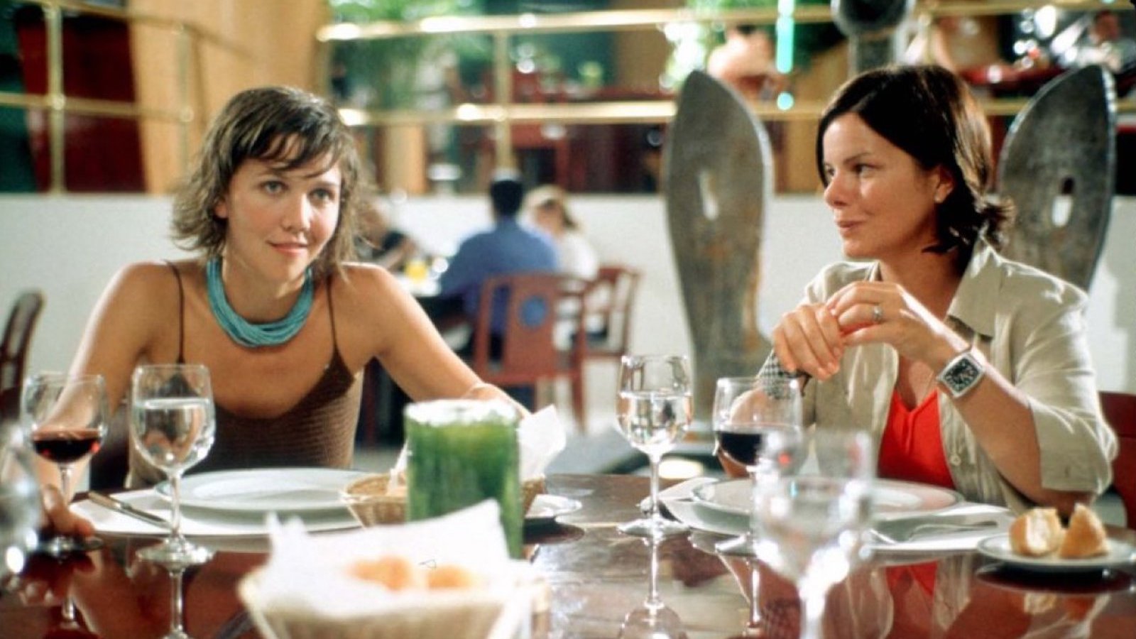 Two women sit at an outdoor table, eating and talking.