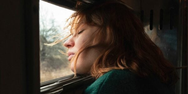 A puts her head near a train window, her eyes closed, wind whipping her hair.