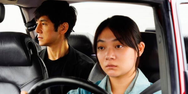 A woman with a serious expression drives a man, who sits in the back seat of the car.