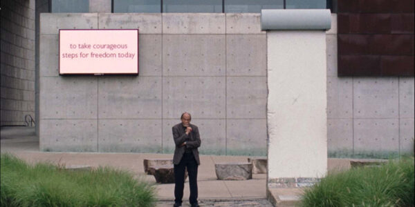 A man stands A man stands in front of a concrete building in front of a sign that says "to take courageous steps for freedom today"