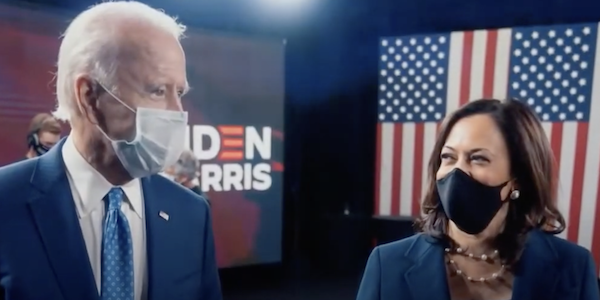 During the presidential campaign, Joe Biden and Kamala Harris, both wearing face masks, stand in front of monitors and an American flag.