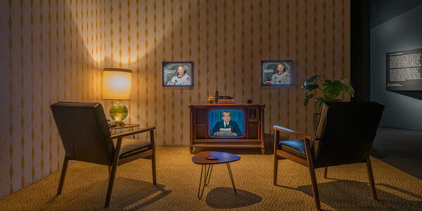 An exhibition mockup of a living room, with two chairs facing a television showing an image of President Nixon giving an address.