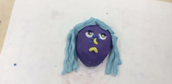 A stop-motion purple clay face of a girl with a frown and tears.