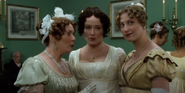 Three women in 19th-century clothes commiserate while at a ball, the woman in the center and the woman on the right looking off-screen past the camera.