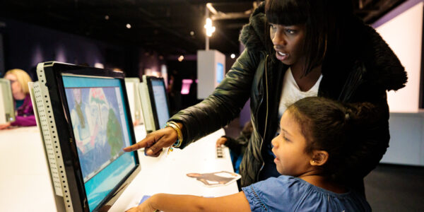 A woman instructs a little girl how to animate at a computer in the Museum