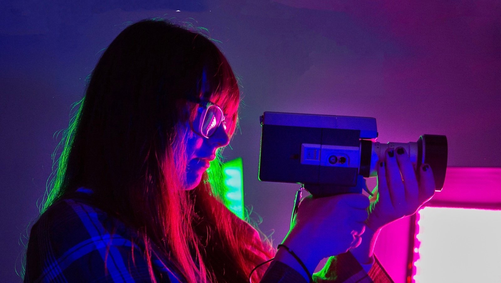 A young woman in profile in glasses looks through the lens of a camera