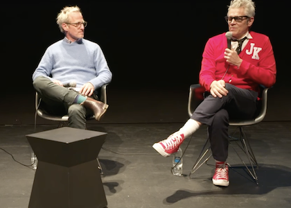 Spike Jonze in white and Johnny Knoxville in red, sitting on stage at the Museum, talking.