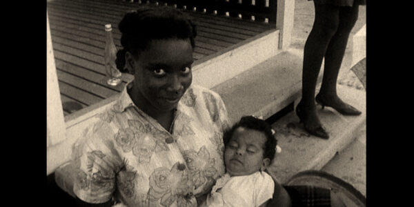 A smiling woman holds a baby and looks into the camera, in a black-and-white image