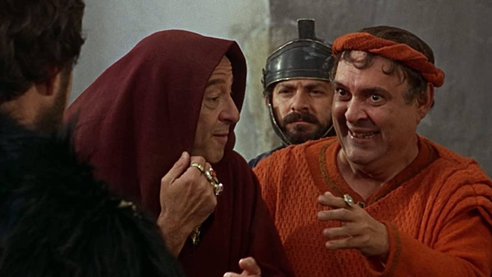 A group of men in ancient Roman garb smile and conspire.