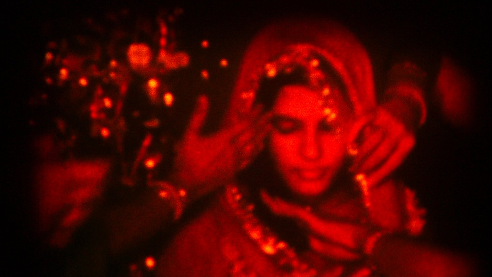 An image of a woman in a sari and veil, with hands surrounding her veil as she looks down