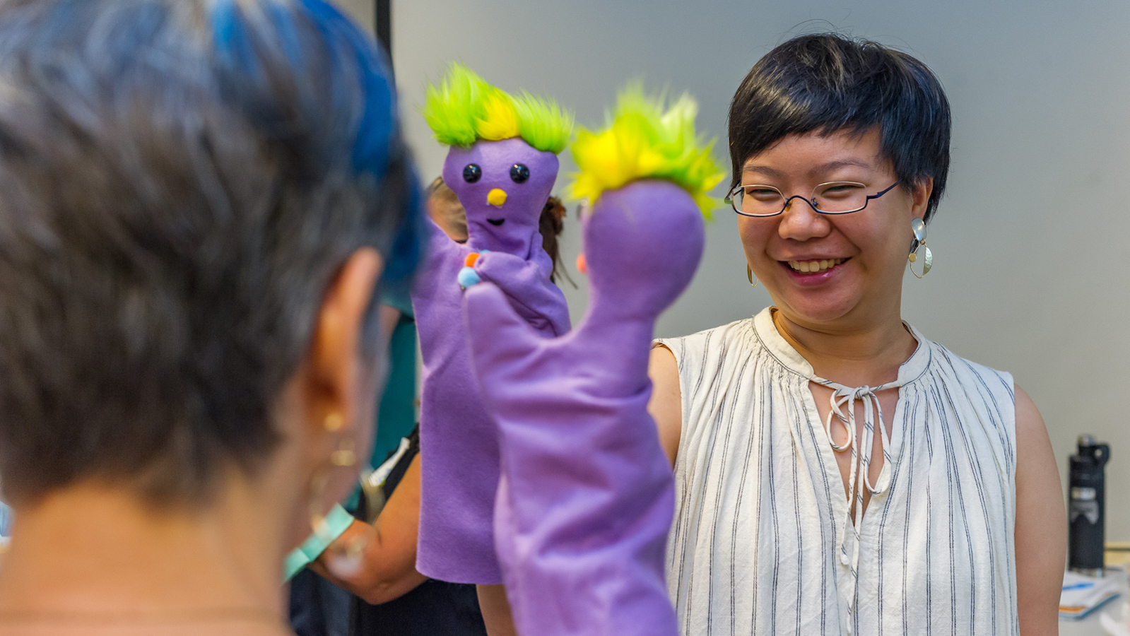 Two women smile and hold purple puppets up to each other