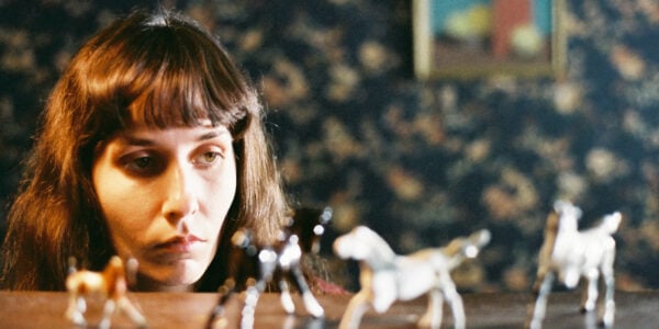 A sullen woman looks at four plastic toy horses on a table