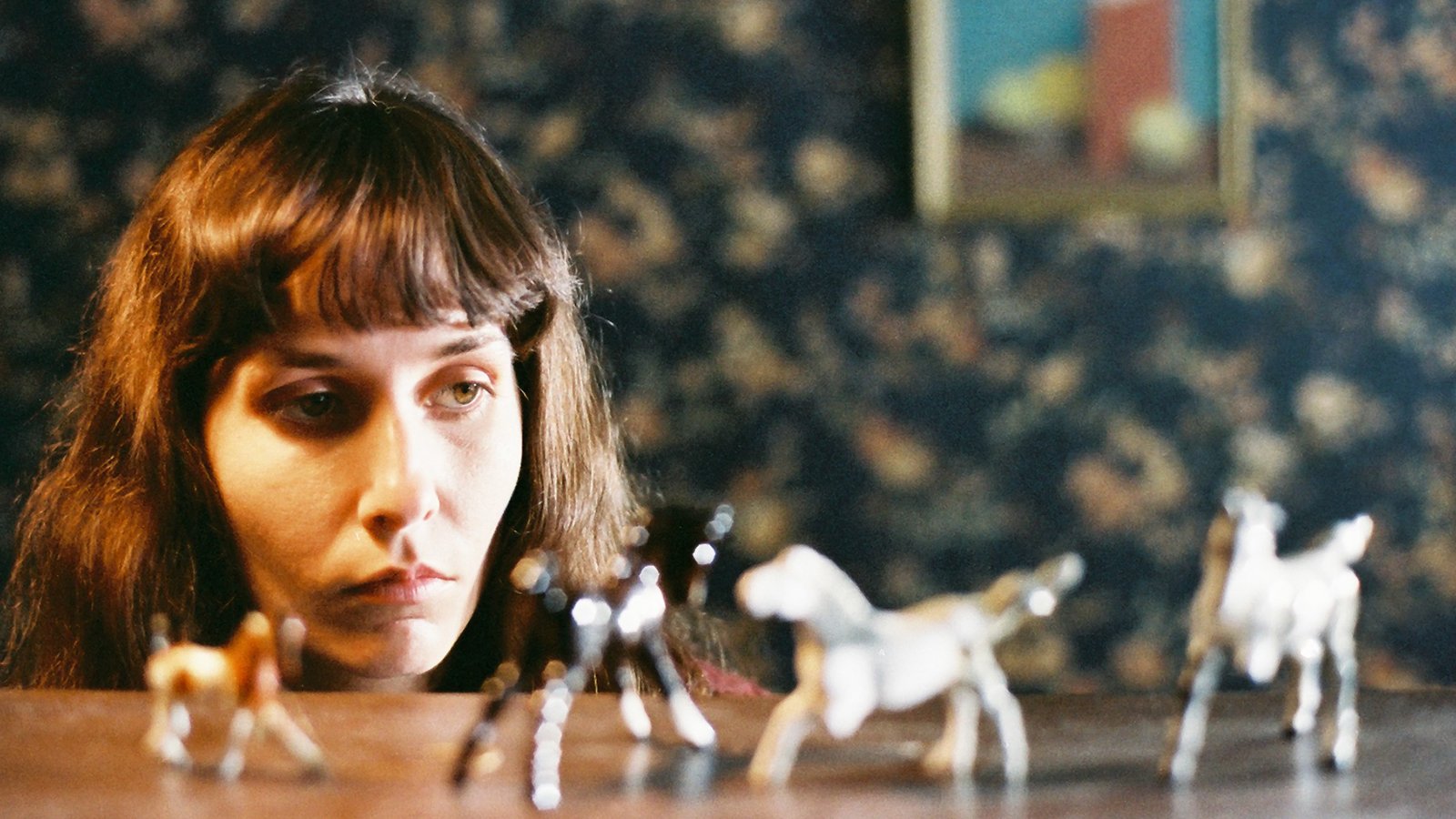 A sullen woman looks at four plastic toy horses on a table