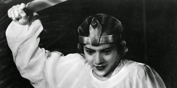 A woman in a metal crown raises a sword and looks down
