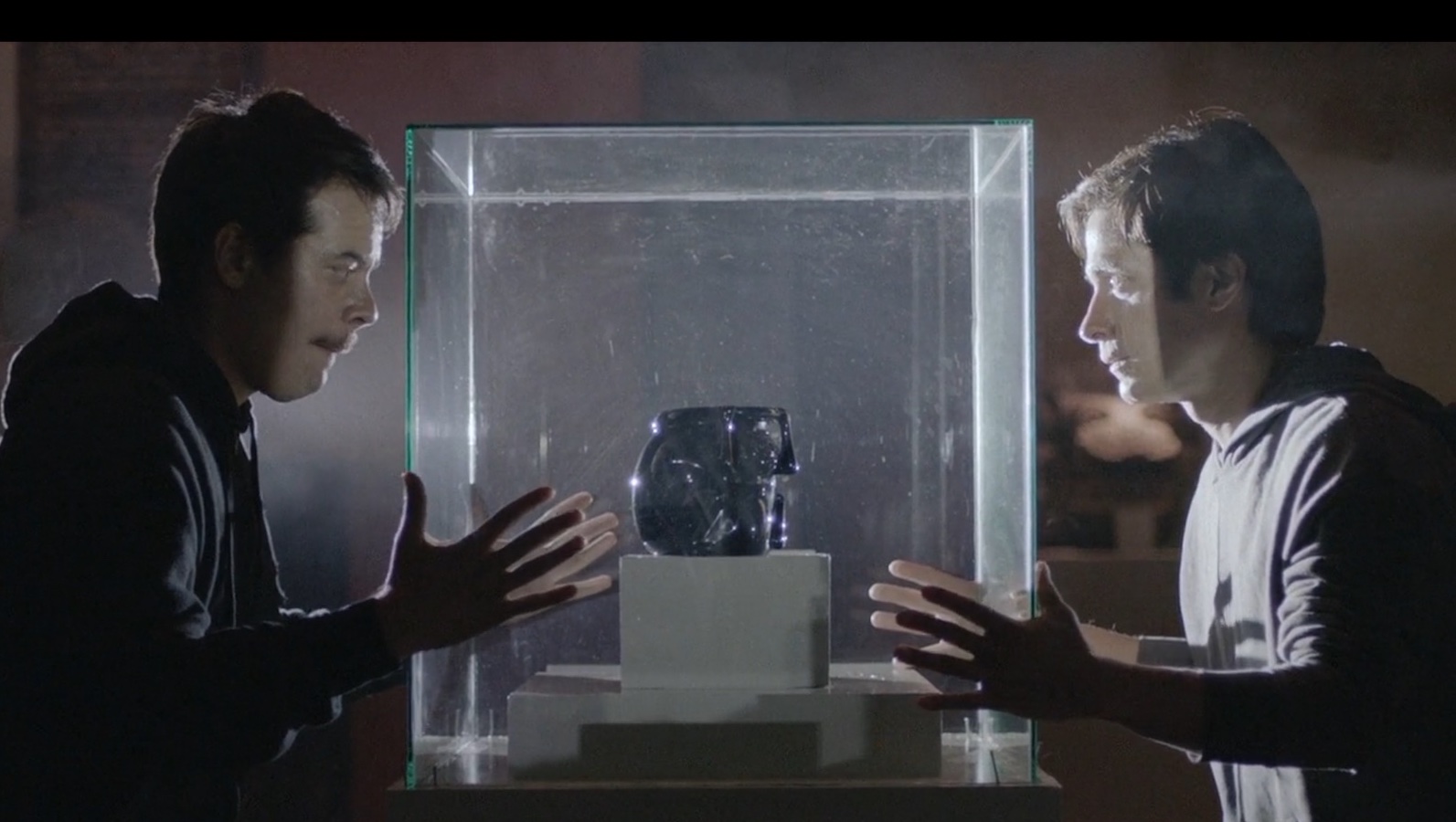 Two young men in a museum at night looking at a mask in a glass case