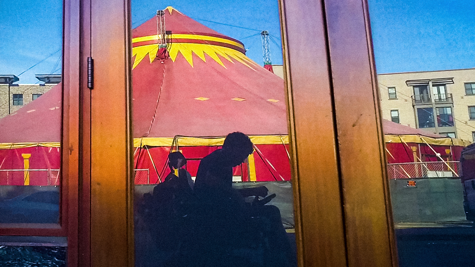 A reflection in a doorway of a man in a wheelchair, set against a red and yellow circus tent