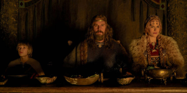 Three members of a Viking family sit in a dark room at a dinner table facing camera