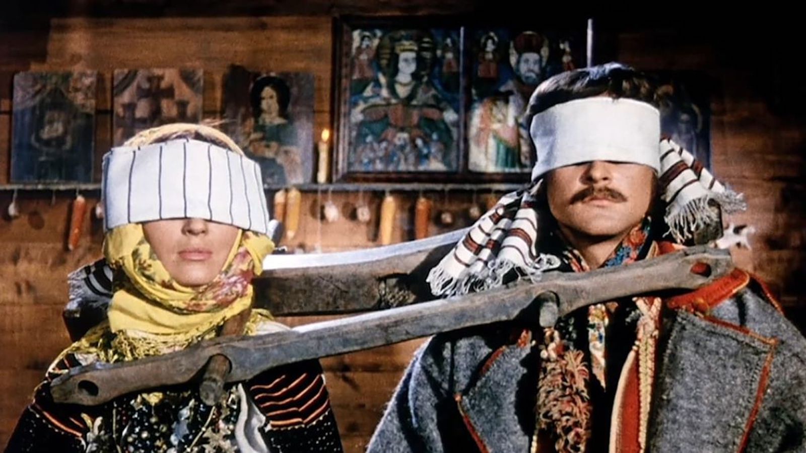 Two blindfolded people stand in wooden stocks around their necks