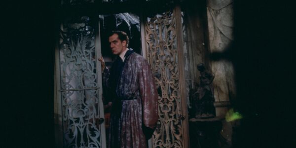 A man in dressing gown looks menacingly at the viewer as he walks through a latticed doorway