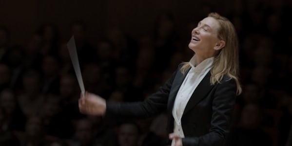 A woman ecstatically conducts an orchestra, holding a baton and wearing a tuxedo.