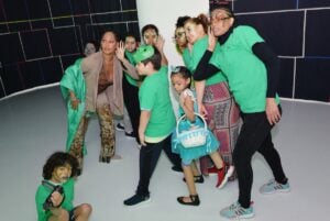 A woman and a group of young people in green shirts dancing and posing for camera