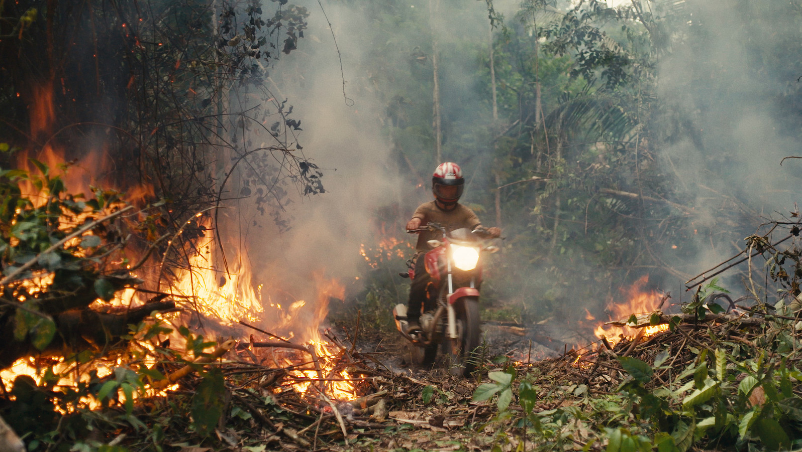 An invader rides his motorcycle through the rainforest fire blaze.