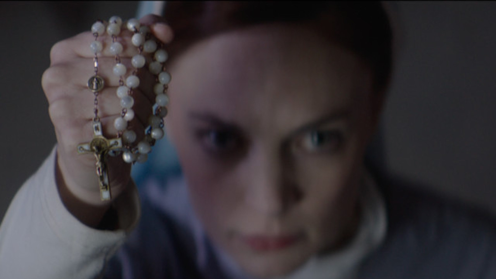A woman holds up a pearly necklace towards the camera in close-up, her face blurred and out of focus