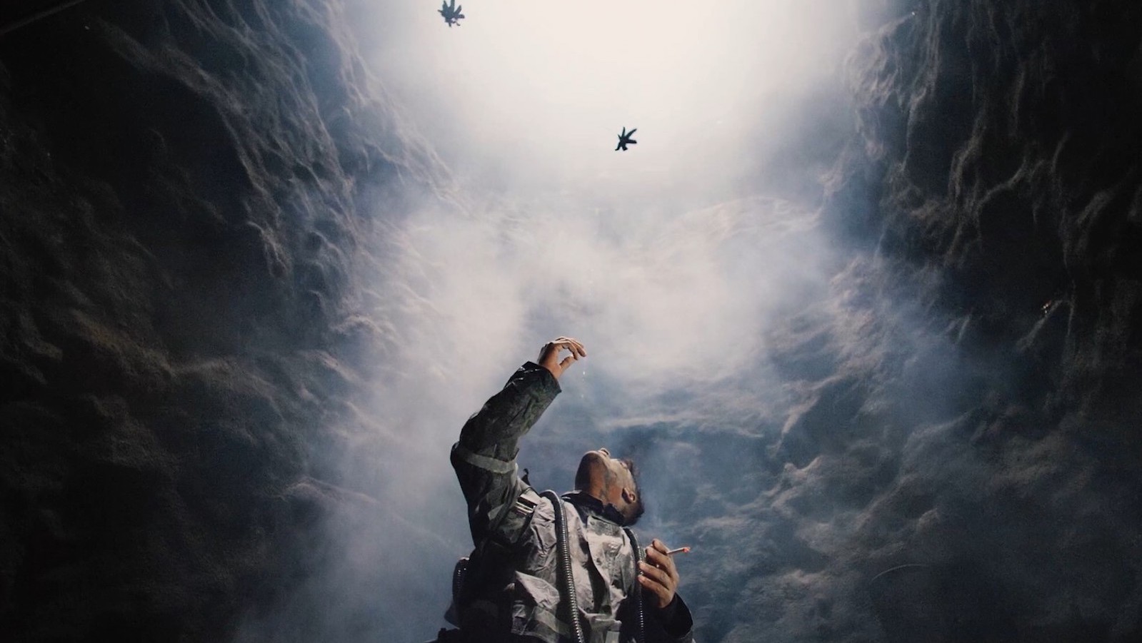 A man reaches up in the middle of a cave at floating leaves above his head