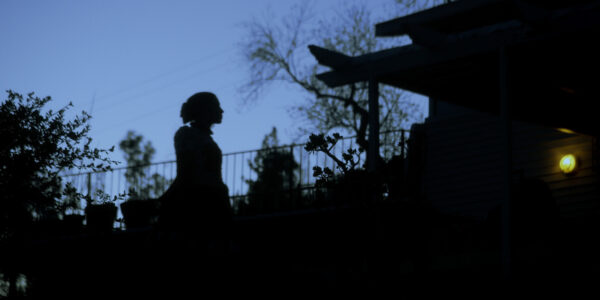A figure walks outside silhouetted against a blue evening sky surrounded by trees