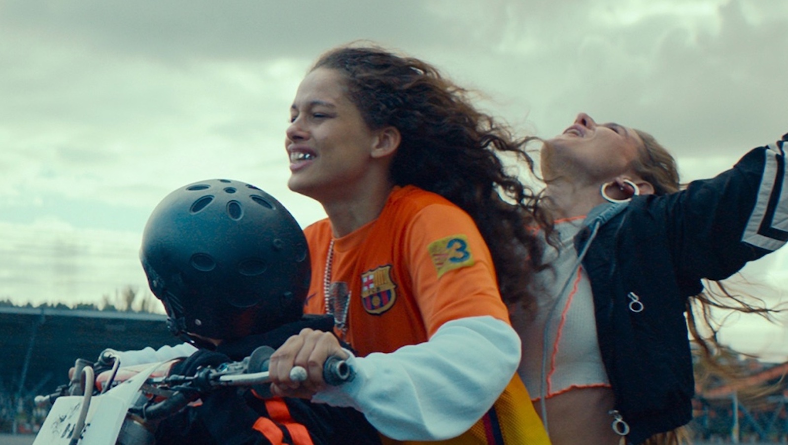 Two young women on a motorcycle, the one in back with arms in air